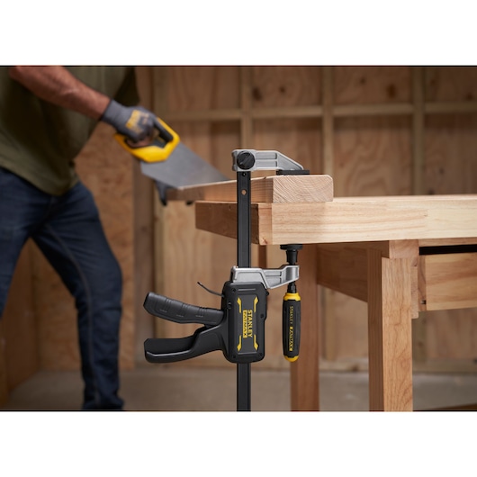 STANLEY® FATMAX® Hybrid Trigger Clamp, 600mmclamping plank of wood to workbench in foreground; wood is sawed in background